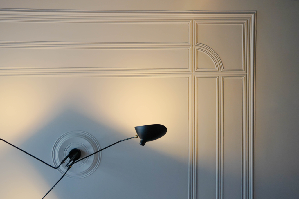 Mooi plafond met origineel lijstwerk, waar een zwarte plafondlamp aan hangt.