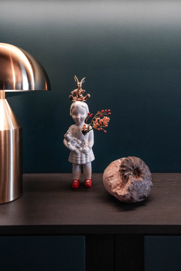 Op een petrol kleurige maatwerkkast staat een popje van Lammers en Lammers met wat bloemen en een groot schelpfossiel